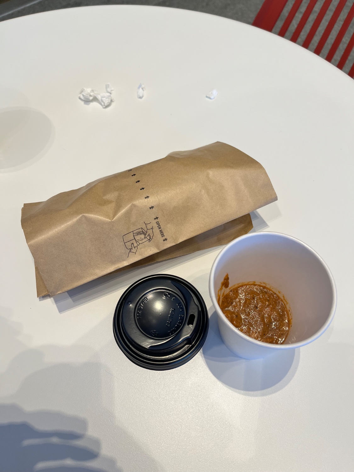 Small white coffee cup full of brown hot sauce next to its lid and wrapped egg burrito. 